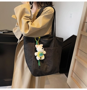 Street style view of a large black denim tote bag with a white plush puppy charm pendant