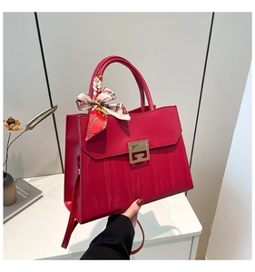 Detailed shot of dark red handbag featuring a gold square twist lock and decorative silk scarf