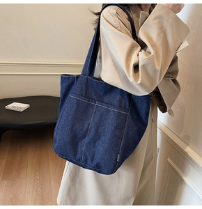 Detail of blue denim tote bag with white stitching and front double pockets
