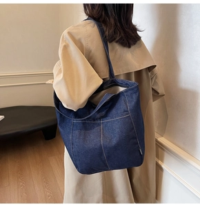 Detail view of large navy denim tote bag with white contrast stitching on model