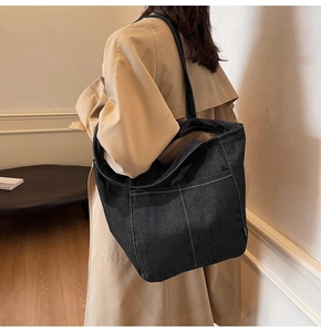 Close-up of a large denim tote bag featuring white contrast stitching and a front pocket