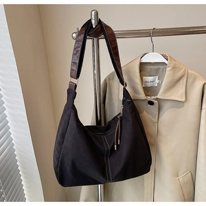 Detail van zwarte canvas tas met contraststiksels en verstelbare bruine lederen riem
