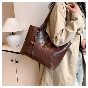 Detail of a dark brown quilted tote bag featuring a metallic turn-lock and charm on the side