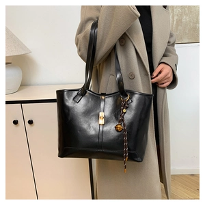 Detail of black leather tote bag featuring a gold twist lock and bell charm pendant