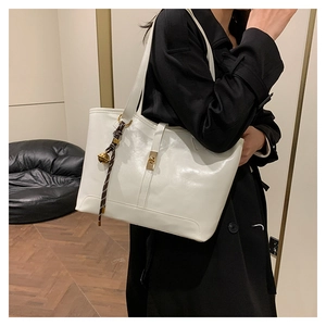 Detail of white glossy tote bag with gold twist lock and striped decorative pendant