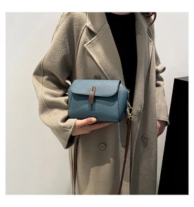 Detail of blue pebble grain leather crossbody bag with brown strap and gold metal hardware