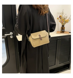 Detail of khaki pebbled leather shoulder bag with dark brown trim and gold metal buckle