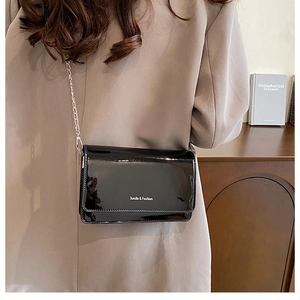 Detail showing high-gloss black patent leather bag with silver chain strap and brand logo
