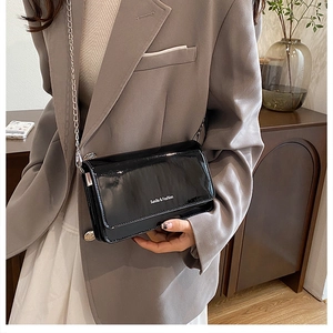 Close-up of black glossy patent leather crossbody bag with silver chain and white text detail