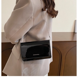 Detail of glossy black patent leather square bag with silver chain strap worn by model