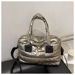 Detail der champagnergoldenen gesteppten Daunentasche mit schwarzen Griffen und Metallglanz