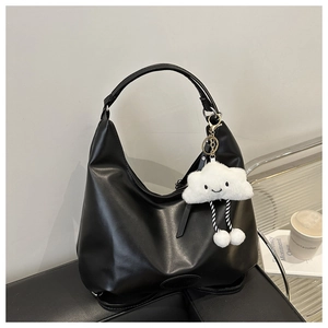 Detail of a black moon-shaped hobo bag with a white plush cloud charm on a leather chair