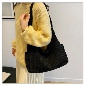 Black corduroy hobo bag styled with a yellow knit sweater and white pleated skirt