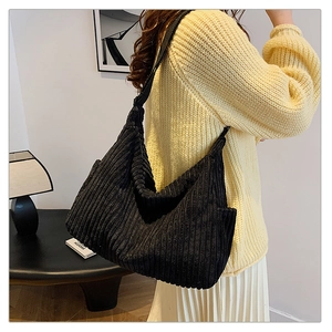 Detail of black corduroy hobo bag showing ribbed texture and wide strap on a model