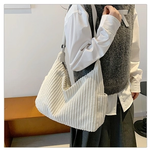 Detail of white corduroy tote bag with side pocket and zipper closure shown on model