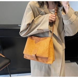 Detail of tan suede shoulder bag featuring a brown leather strap and flap buckle closure