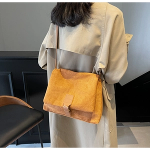 Dettaglio della borsa a tracolla in pelle scamosciata senape indossata con un trench beige