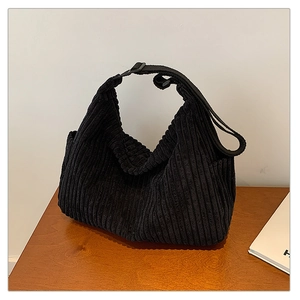 Close-up of black corduroy hobo bag texture with adjustable strap on wooden table