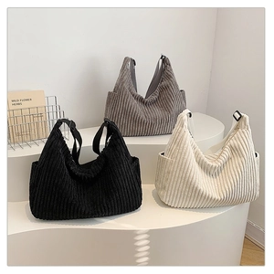 Three corduroy tote bags in black, taupe and white on display stands with wide straps