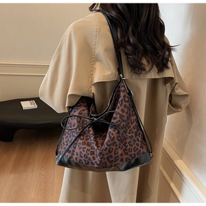 Detail of trendy leopard print tote bag featuring a bow accent and black leather straps
