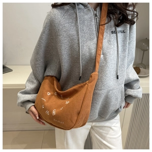 Close-up of brown corduroy crescent bag with letter embroidery and adjustable strap