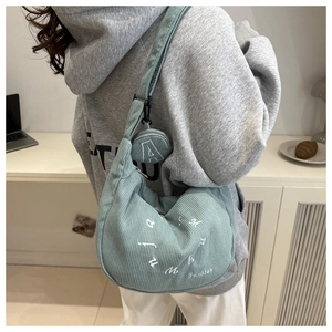 Detail of grey-green corduroy crescent tote bag with white embroidery and mini pouch