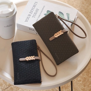 Detail of long leather wallets with leaf metal clasp and wristlet on a white table