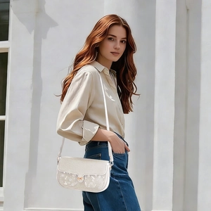 Detail of white leather crossbody bag with subtle patterns and a golden buckle closure