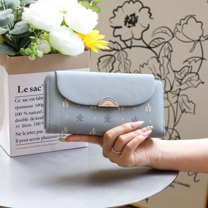 Close-up of light blue trifold wallet featuring leaf prints and golden metal buckle
