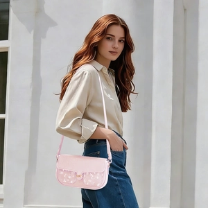 Detail of pink crossbody bag featuring white floral patterns and a gold metal buckle