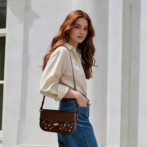 Detail of dark brown leather crossbody bag with geometric prints and gold metal buckle