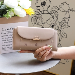 Close-up of beige leaf-print trifold wallet featuring a golden semi-circular metal clasp