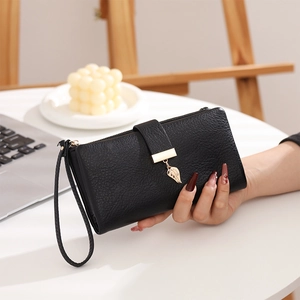 Detalle de cartera negra para mujer con colgante de hoja y correa de muñeca