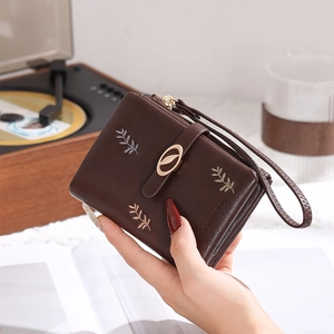 Detail of short leather wallet with leaf embroidery, wrist strap, and golden buckle