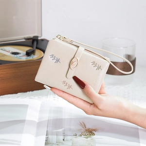Close-up of beige wallet featuring elegant leaf embroidery and a gold leaf-shaped clasp