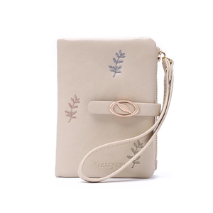 Detail of beige faux leather wallet with floral leaf embroidery and leaf metal clasp