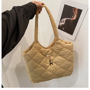 Detail of khaki quilted tote bag featuring a gold metal tag and black deer charm