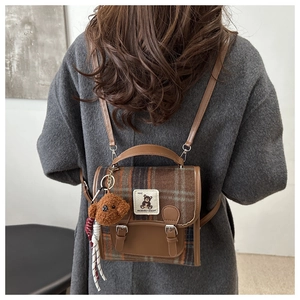 Detail of plaid backpack featuring brown faux leather trim and plush bear charm accent