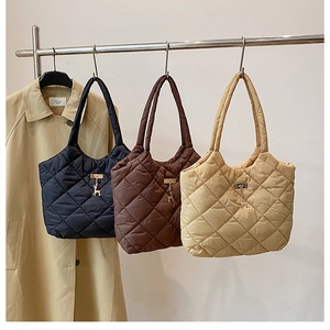 Quilted tote bags in black, brown, and beige with deer charm on display stand