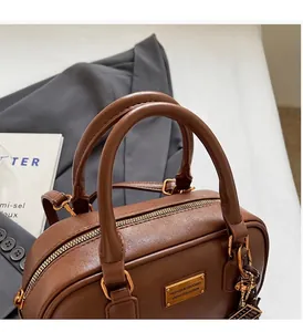 Detail einer braunen Kunstledertasche mit robusten Griffen und goldenem Metallreißverschluss