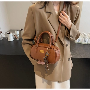 Nahaufnahme der braunen Retro-Zylindertasche aus Leder mit Goldplakette und Bandverzierung