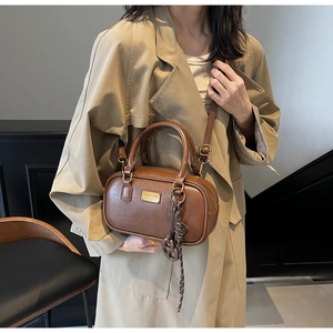 Detail einer braunen Boston-Tasche mit Herzanhänger an einem beigen Trenchcoat