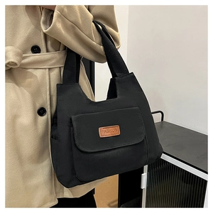 Dettaglio della borsa tote in tela nera con tasca anteriore e toppa con logo moda