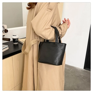 Close-up of black soft leather tote bag with vintage texture on woman in beige coat
