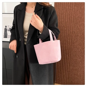 Detail of pink minimalist soft leather handbag held by model in black wool coat