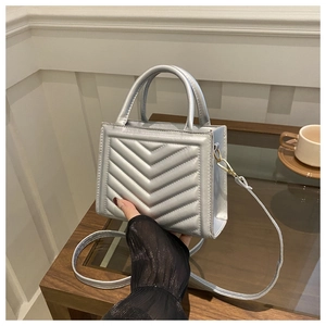 Detailed shot of silver V-quilted faux leather handbag with golden hardware and twin handles