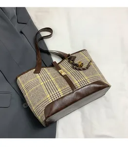 Detail of plaid tote bag with brown leather trim and golden buckle on grey blazer