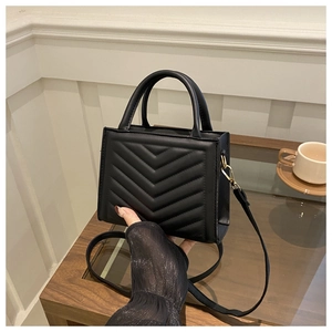 Detail of black quilted leather ladybag with gold metal hooks on a wooden table