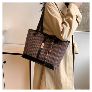Detail of vintage plaid tote bag with black leather straps and golden twist lock closure