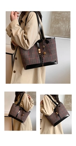 Detail of red and black plaid wool tote bag with leather trim and decorative bag charm